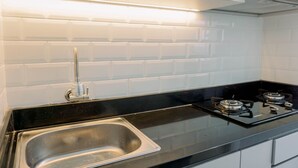 A modern kitchen with white subway tiles, stainless steel sink, black countertop, and two gas stoves. - Cozy Stay Studio At Urbantown Serpong Apartment (South Tangerang)