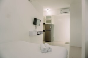 A hotel room with a bed, a TV mounted on the wall, a refrigerator, and a microwave.