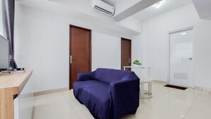 A room with a blue sofa, a wooden desk, a small white table, and a door. - Restful And Modern 2Br Majestic Point Serpong Apartment (Gading Serpong)