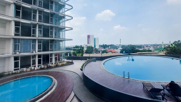 A rooftop swimming pool with a view of a modern building and a mosque in the background. - Restful And Modern 2Br Majestic Point Serpong Apartment (Gading Serpong)