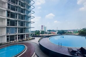 A rooftop swimming pool with a view of a modern building and a mosque in the background. - Restful And Modern 2Br Majestic Point Serpong Apartment (Gading Serpong)