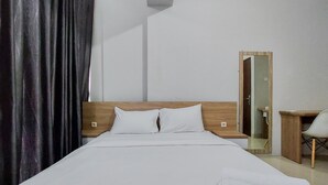 A hotel room with a bed, a wooden headboard, a desk with a chair, and a mirror. - Restful And Modern 2Br Majestic Point Serpong Apartment (Gading Serpong)