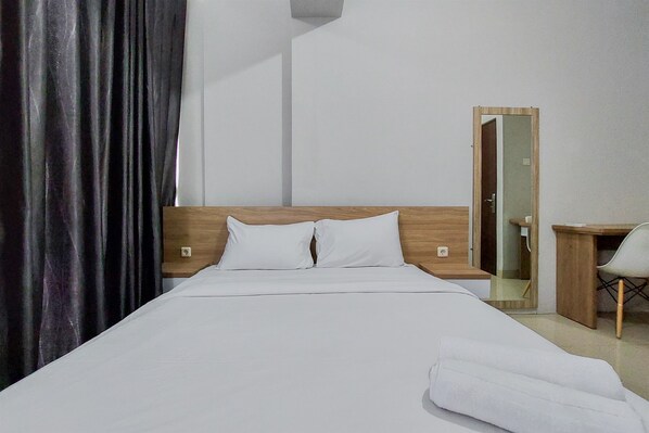A hotel room with a bed, a wooden headboard, a desk with a chair, and a mirror. - Restful And Modern 2Br Majestic Point Serpong Apartment (Gading Serpong)