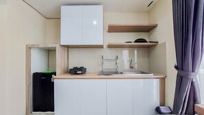 A compact kitchen with white cabinets, a sink, and a small refrigerator. - Restful And Modern 2Br Majestic Point Serpong Apartment (Gading Serpong)