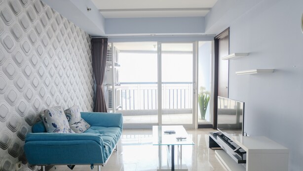 A modern living room with a blue sofa, a glass coffee table, and a flat-screen TV. - Homey And Cozy 1Br Apartment At Braga City Walk (Bandung)
