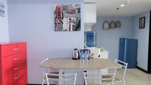 A dining area with a wooden table, white chairs, a red cabinet, a blue water dispenser, and a refrigerator. - Homey And Cozy 1Br Apartment At Braga City Walk (Bandung)