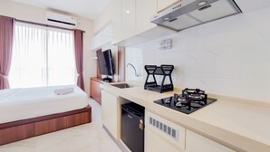 A modern hotel room with a bed, a small kitchenette, a TV, and an air conditioning unit.