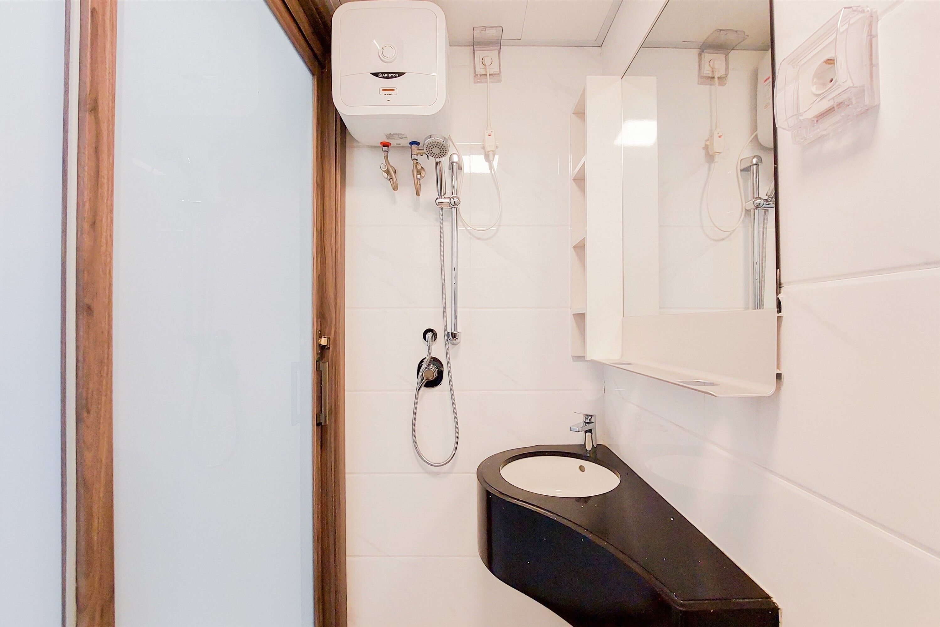 A small bathroom with a white tiled wall, a black sink, a mirror, and a shower with a handheld showerhead.