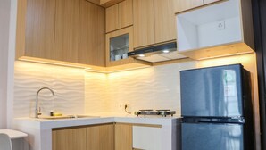 A compact kitchen with wooden cabinets, a stainless steel refrigerator, a built-in oven, and a microwave. - Brand New 2BR at Daan Mogot City Apartment By Travelio (Jakarta)
