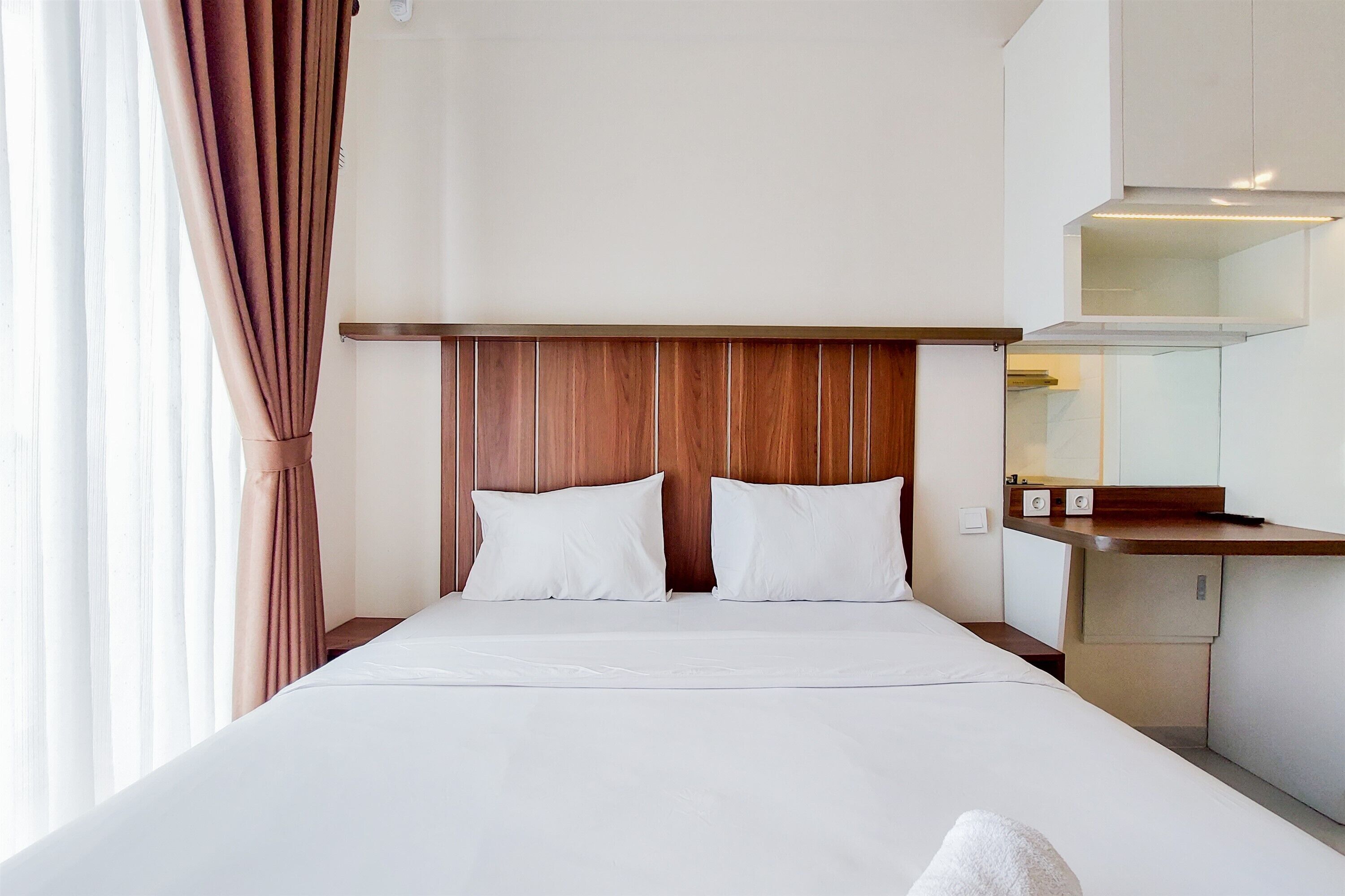 A hotel room with a wooden headboard, a bed with white linens, a small bedside table, and a mirror above it.
