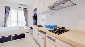 A compact hotel room with a bed, kitchenette, and a window with curtains. - Fancy And Nice Studio At 20Th Floor Sky House Bsd Apartment (Pagedangan)
