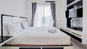 A modern hotel room with a large bed, a flat-screen TV, and an air conditioning unit. - Fancy And Nice Studio At 20Th Floor Sky House Bsd Apartment (Pagedangan)