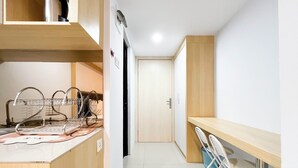A narrow hallway with a wooden desk and chairs, a metal rack, and a door at the end. - Modern Look Studio At De Prima Apartment (Medan)