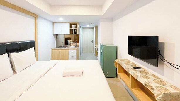 A hotel room with a bed, a TV, a small kitchenette, and a bathroom visible in the background. - Modern Look Studio At De Prima Apartment (Medan)