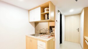 A compact kitchen with a sink, a dish rack, and wooden cabinets. - Modern Look Studio At De Prima Apartment (Medan)