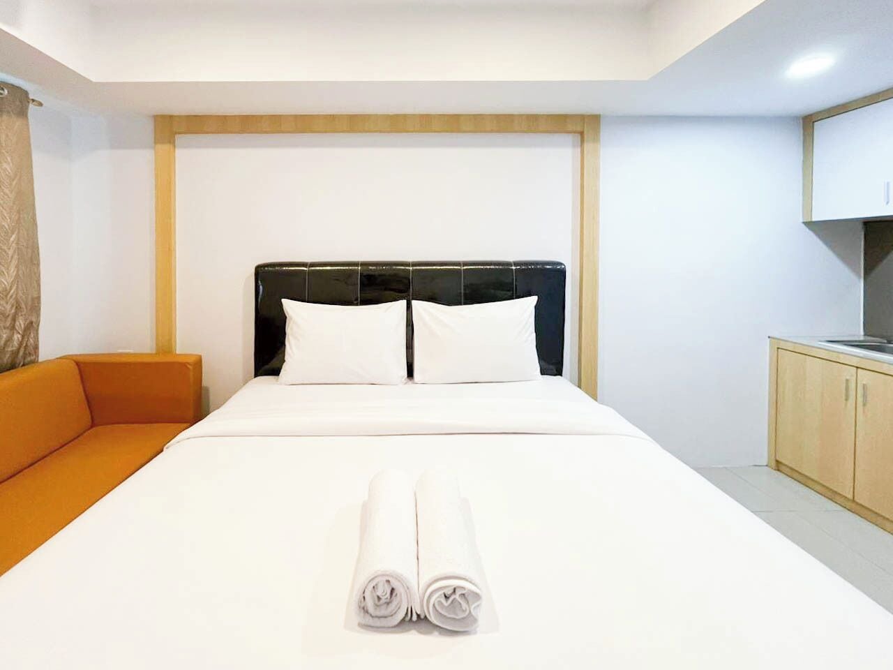 A hotel room with a large bed, a wooden headboard, an orange sofa, and a kitchenette.