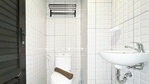 A bathroom with white tiled walls, a white toilet, a sink with a chrome faucet, and a towel rack above the toilet. - Modern Look Studio At De Prima Apartment (Medan)