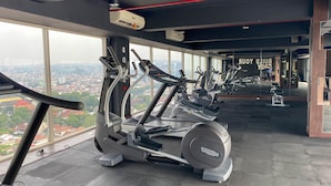 Une salle de sport équipée de tapis de course et d’appareils d’exercice, de grandes fenêtres offrant une vue sur la ville et d’un murmiroir qui reflète l’équipement.