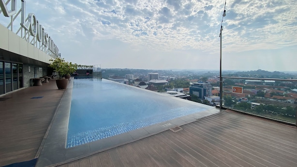 Une piscine à débordement située sur le toit, offrant une vue sur la ville, avec une terrasse en bois et un espace salon extérieur.
