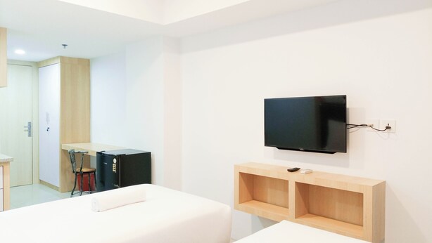 A hotel room with two beds, a TV mounted on the wall, and a wooden shelf. - Cozy Studio Room At De Prima Apartment (Medan)