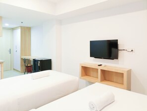 A hotel room with two beds, a TV mounted on the wall, and a wooden shelf. - Cozy Studio Room At De Prima Apartment (Medan)