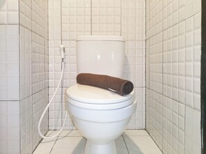 A toilet with a brown towel on top, a white toilet seat, and a white toilet tank. - Cozy Studio Room At De Prima Apartment (Medan)