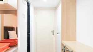 A narrow hallway with a door at the end, a small seating area with a chair, and a countertop with a red container. - Cozy Studio Room At De Prima Apartment (Medan)