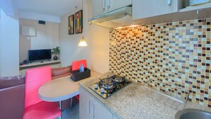 Una cocina compacta con estufa a gas, una pequeña mesa de comedor y una silla roja.