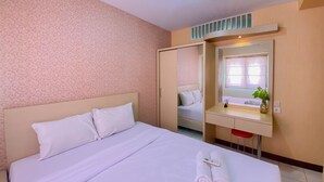 Habitación de hotel con una cama grande, una mesita de noche con espejo, un taburete pequeño y una ventana con una planta sobre el tocador.