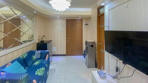 A modern living room with a sofa, a flat-screen TV, a water dispenser, and a ceiling light fixture. - Fancy And Nice 2Br At Cinere Resort Apartment (Depok)