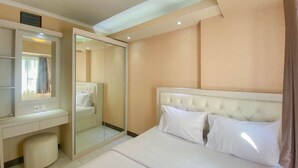 A hotel room with a bed, a vanity with a mirror, a small stool, and a walk-in closet. - Fancy And Nice 2Br At Cinere Resort Apartment (Depok)