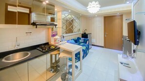 A modern kitchen with a sink, stove, and bar stools. There is a dining area with a blue sofa and a TV. - Fancy And Nice 2Br At Cinere Resort Apartment (Depok)