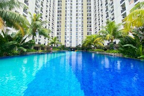 A swimming pool surrounded by tall residential buildings and palm trees. - Fancy And Nice 2Br At Cinere Resort Apartment (Depok)