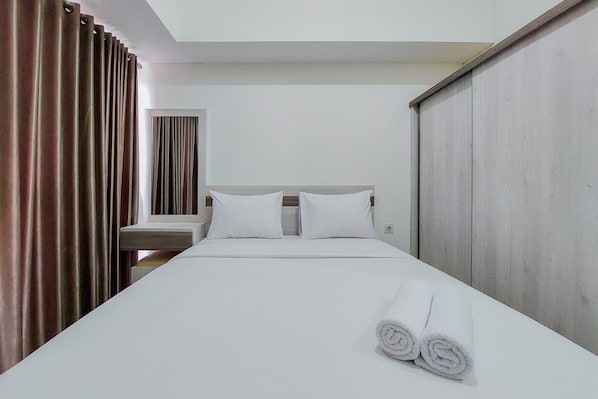 Ein Hotelzimmer mit einem Bett, zwei Kissen, einem Nachttisch und einem aufgerollten Handtuch auf dem Bett.