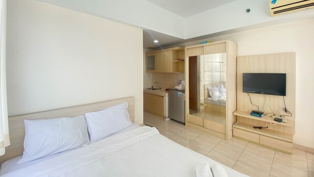 A hotel room with a bed, a TV mounted on the wall, a kitchenette, and an air conditioning unit. - Homey And Cozy Stay Studio Margonda Residence 3 Apartment (Depok)