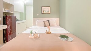 A bedroom with a bed, bedside table, and a small plant. There is a kitchen area visible in the background. - Cozy Stay Studio At 3Rd Floor Springlake Summarecon Bekasi Apartment (Bekasi)