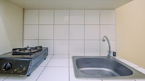 A small kitchen with a gas stove, a sink, and white tiled walls. - Cozy Stay Studio At 3Rd Floor Springlake Summarecon Bekasi Apartment (Bekasi)