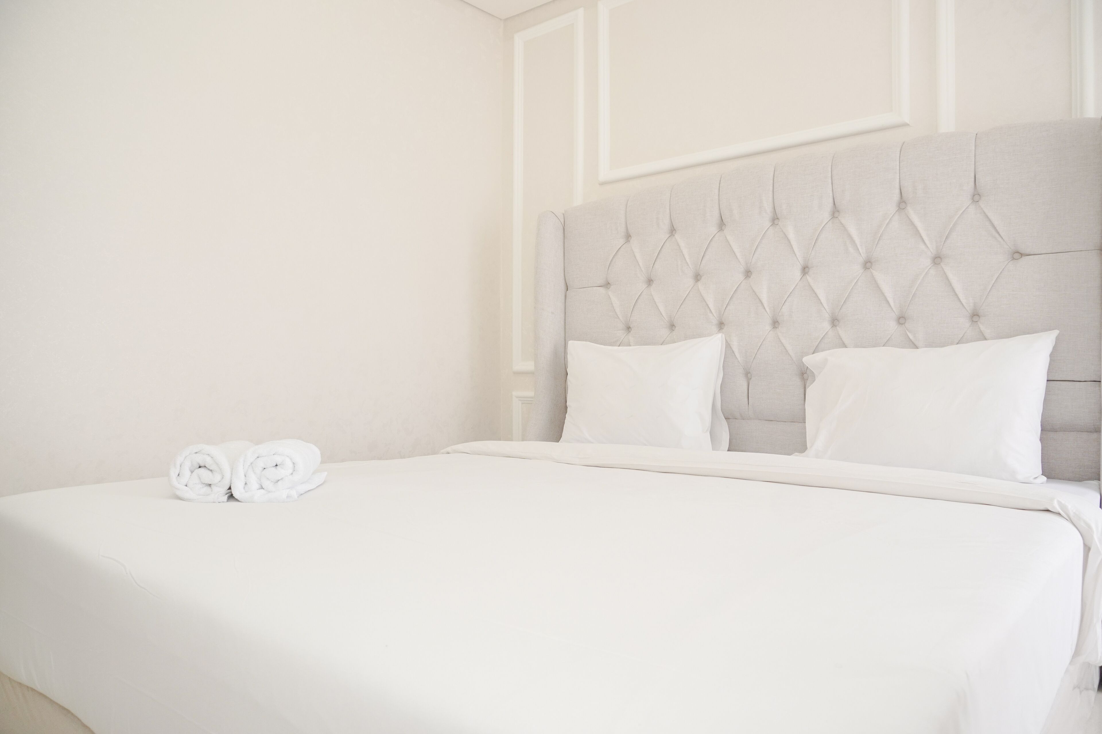 A neatly made bed with a tufted headboard and two rolled towels on the bed.