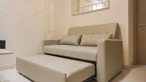 Una habitación moderna y minimalista con un sofá y reposapiés color beige, una mesita auxiliar pequeña y un espejo montado en la pared.