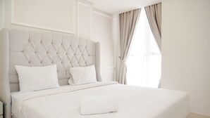 Una cama bien hecha con cabecera tapizada, ropa de cama blanca y una toalla doblada.