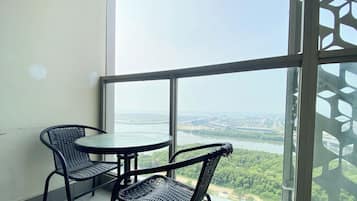 A balcony with two wicker chairs and a small round table, overlooking a river and cityscape.