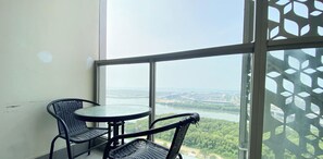 Balcón con dos sillas de mimbre y una pequeña mesa redonda, con vistas a un río y al paisaje urbano.