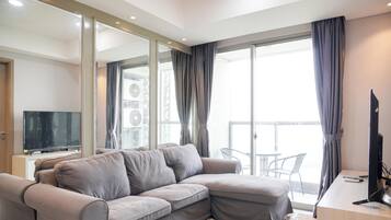A modern living room with a grey sectional sofa, a flat-screen TV, a wooden desk, and a balcony with a view.