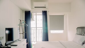 A hotel room with a bed, a desk with a computer, a TV, and a window with curtains. - Minimalist And Best Deal Studio At Serpong Garden Apartment (Cisauk)