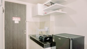 A compact kitchen with a refrigerator, a microwave, and a sink. There is a wooden door and a white shelf above the counter. - Minimalist And Best Deal Studio At Serpong Garden Apartment (Cisauk)