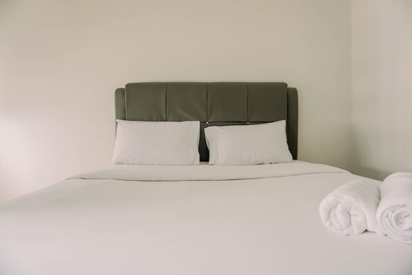 A neatly made bed with a green upholstered headboard, white bedding, and a rolled white towel on the side. - Minimalist And Best Deal Studio At Serpong Garden Apartment (Cisauk)