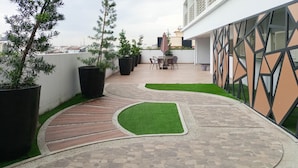 A rooftop patio with potted plants, a table with chairs, and a geometric wall design. - Simply Look Studio At 21St Floor De Prima Apartment (Medan)