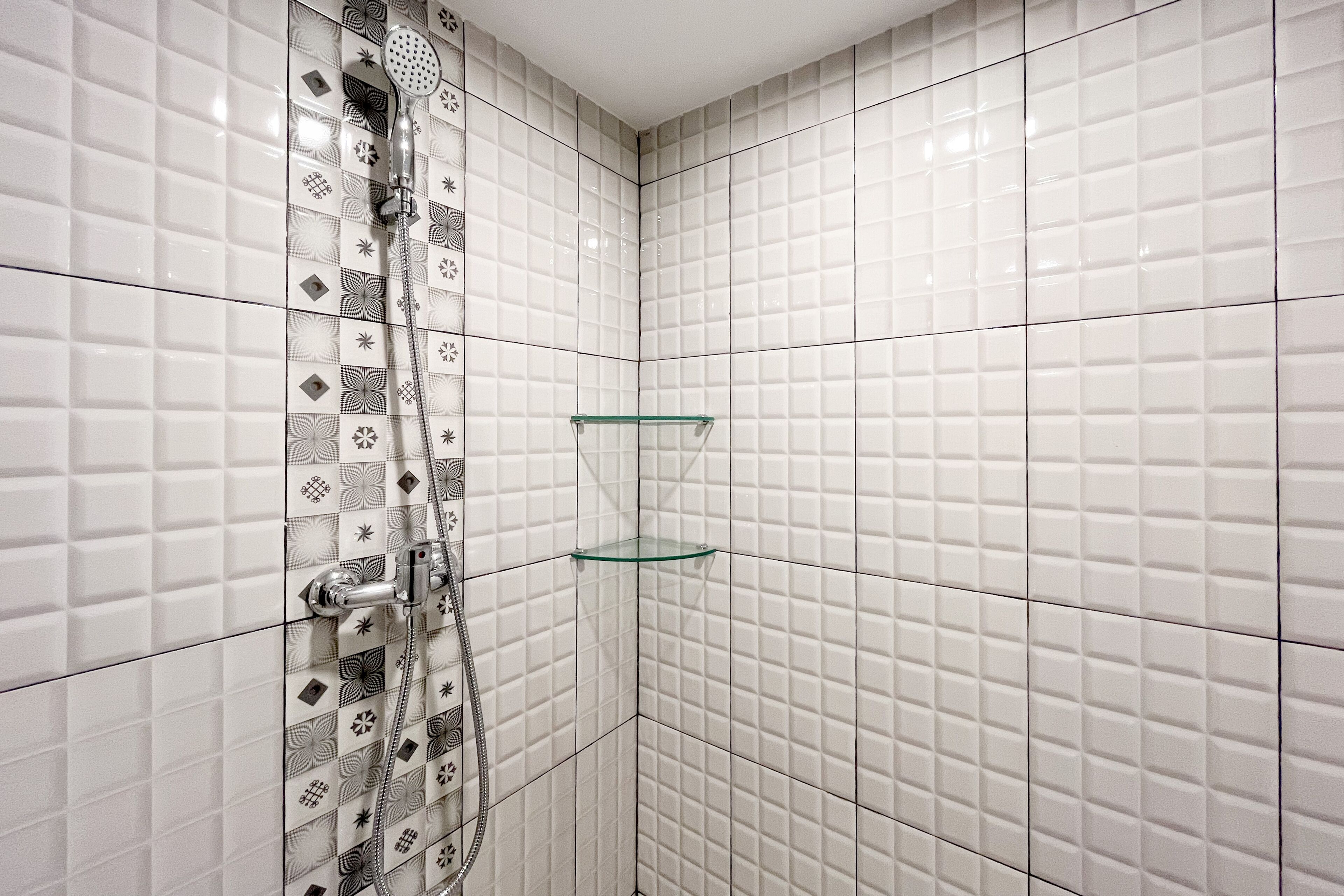 A shower area with white tiles and a glass shelf.