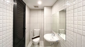 A modern bathroom with white tiled walls, a black door, a toilet, and a sink with a mirror.