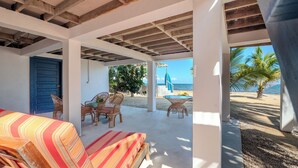 A beachside room with a bed, wicker chairs, and a view of the beach and ocean. - Entire Beach Home w/ Sunroom, Pool, Bikes, Paddleboards, BBQ & more (Hopkins)